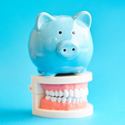 blue piggy bank atop model teeth signifies cost of dental implants in Calimesa