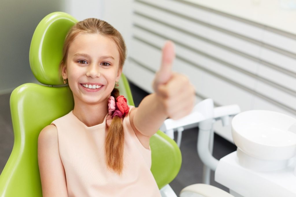 kid with dental sealants smiling and doing thumbs up at dentist