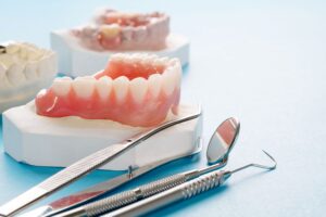 Set of dentures next to dental tweezers and mirror